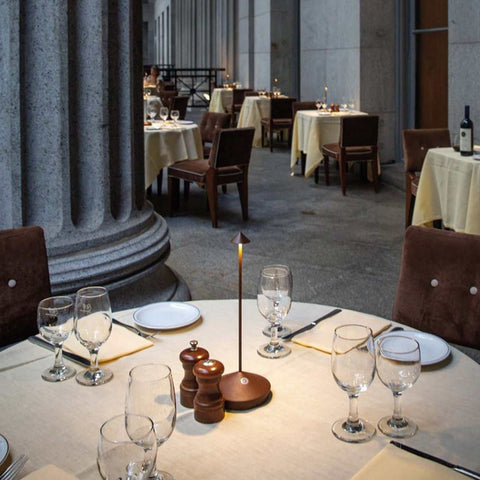 Zafferano Pina Pro rechargeable rust table lamp on a restaurant dining table with glassware and cutlery