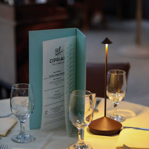 Zafferano Pina Pro rechargeable rust table lamp on a dining table with glassware and menu, providing warm ambient lighting