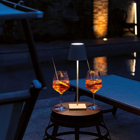 Zafferano Poldina Micro rechargeable sand finish table lamp on outdoor table with two drinks at night