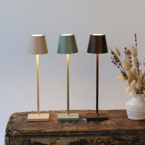 Zafferano Poldina Micro rechargeable sand finish table lamps in beige, green, and brown on rustic wooden surface with dried floral arrangement