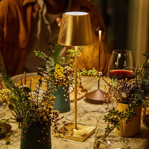 Zafferano Poldina Pro rechargeable gold table lamp on dining table with warm ambient lighting and decorative plants