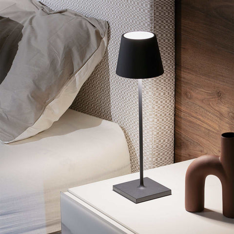 Zafferano Poldina Pro black rechargeable table lamp on bedside table emitting warm light