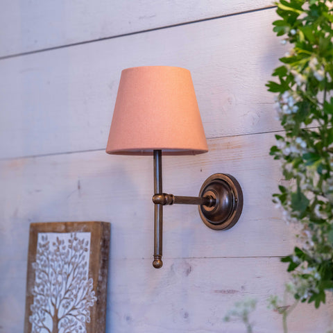 Finberry fabric shade Lupin wall light with pink fabric shade and antique bronze fitting mounted on white wooden wall.