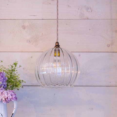 Soho large ribbed glass shade pendant light with clear ribbed globe design hanging in a bright room with wooden wall background and floral arrangement.