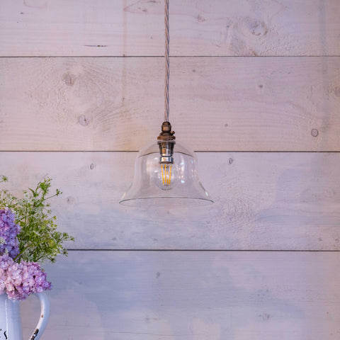 Bodium Small Clear glass pendant light with exposed filament bulb hanging against a white wooden wall above a vase of purple flowers