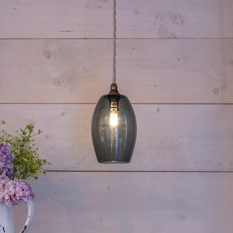 Camber Small Smoked Glass Shade pendant light hanging with warm bulb and flowers on wooden background