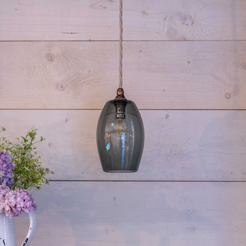 Camber Small Smoked Glass Shade pendant light hanging against white wooden wall with flowers nearby