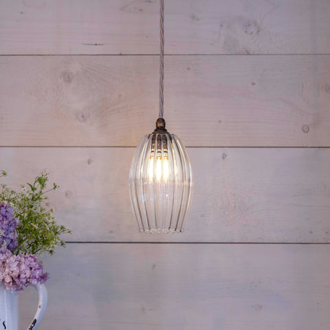Camber Small Ribbed Glass Shade pendant light hanging in a cozy room with soft illumination and rustic wooden background