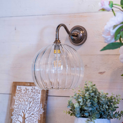Soho Large Ribbed Glass Shade wall light with bronze finish mounted on wooden wall above decorative plants and framed artwork