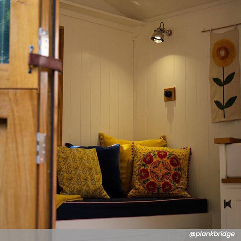 Foxton Adjustable Spotlight by Chehoma mounted on white paneled wall above a cozy seating area with colorful cushions and wooden door in foreground