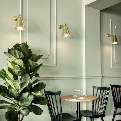 Moya Brass Wall Light with adjustable arm and cone-shaped shade, mounted on wall above dining table in modern dining area