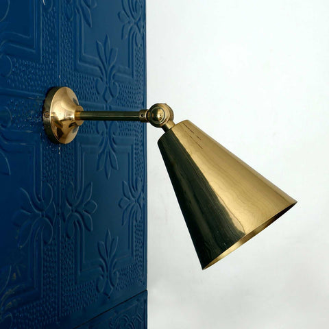 Moya Brass Wall Light with adjustable arm and cone-shaped shade mounted on dark textured wall