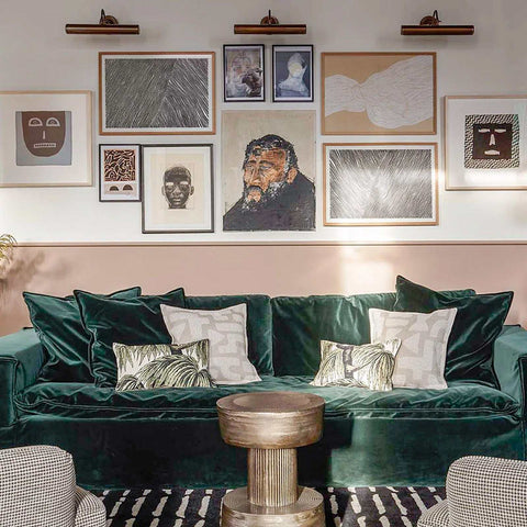 Dublin Picture Light brass wall-mounted light illuminating gallery wall above green velvet sofa in stylish living room