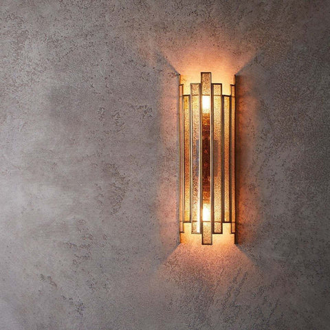 Pooky Tall Melville vintage glass wall light with antique brass finish and Art Deco design emitting warm glow on textured wall