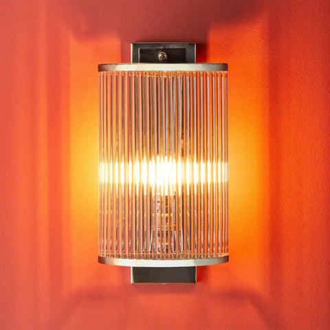 Pooky Roddy Wall Light with clear glass rods in brushed nickel finish on orange wall providing warm ambient lighting