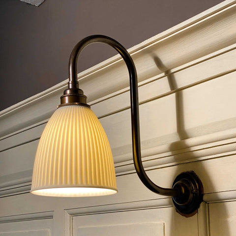 Hartlip small ribbed ceramic shade wall light with bronze curved arm and warm glow mounted on beige paneled wall