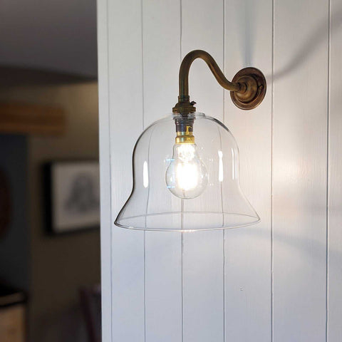 Bodium Medium Clear Glass wall light with handblown clear glass shade and antique brass finish mounted on white wall