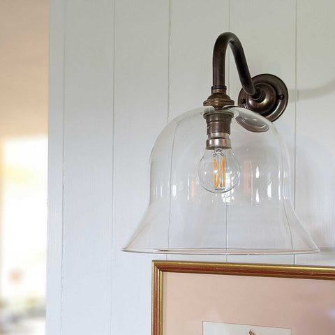 Bodium large clear glass wall light with vintage bronze finish and exposed filament bulb mounted on white paneled wall