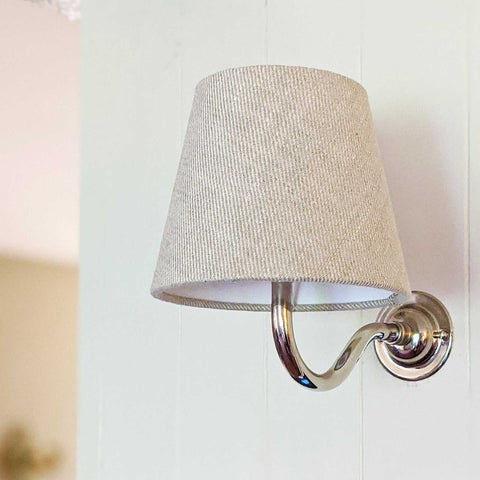 Wall light with natural linen fabric shade and chrome curved arm mounted on white wall