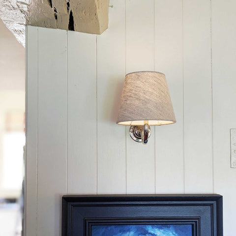 Wall light with natural linen fabric shade mounted on white wooden wall above black framed artwork