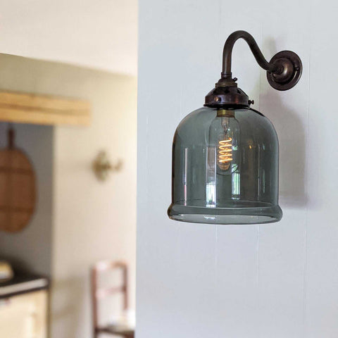 Hythe Small Smoked Glass Shade Wall Light with vintage filament bulb and bronze curved arm mounted on white wall in modern interior