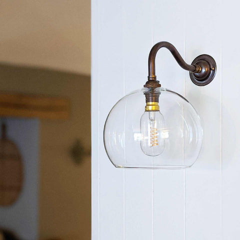 Soho medium clear glass shade wall light with antique brass finish and hand-blown globe design mounted on white wall