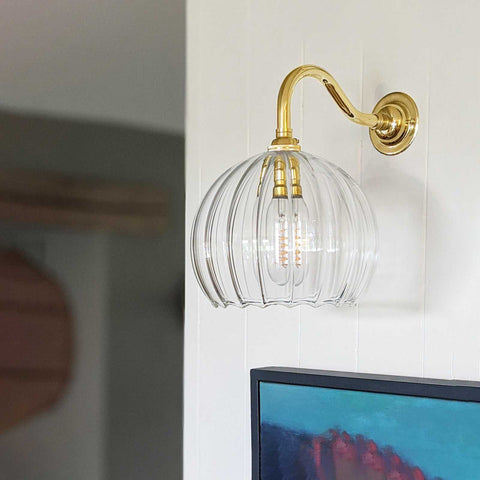 Soho Medium Ribbed Glass Shade wall light with brass swan neck mount on white wall above a painting