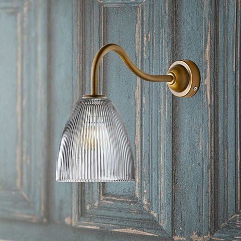 Pooky Tiny Qilin bathroom wall light with swan neck brass arm and prismatic glass shade on textured blue wall