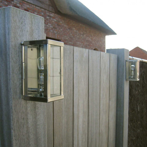 Chiswick Outdoor Wall Light in polished cast brass mounted on wooden fence panels for stylish outdoor illumination