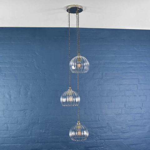 Soho Medium Ribbed Glass 3 Cluster Shade Pendant Light with clear ribbed glass globes hanging against a blue brick wall