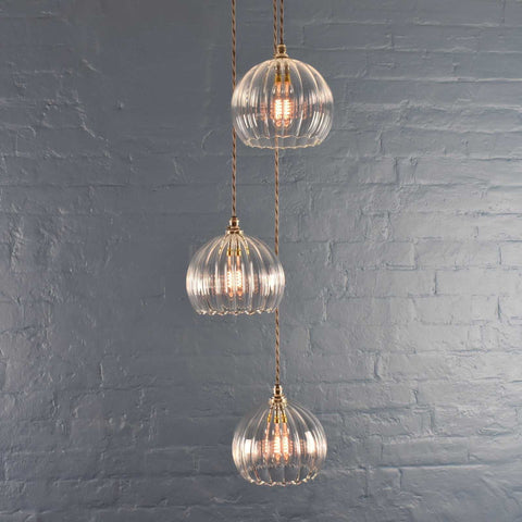 Soho Medium Ribbed Glass 3 cluster pendant light with hand-blown glass shades and adjustable cords against a grey brick wall background