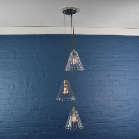 Rye medium ribbed glass shade cluster pendant light with three hand-blown glass shades and adjustable cords against blue brick wall