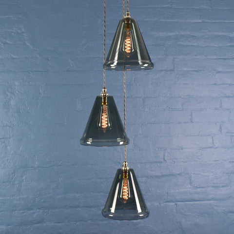 Rye medium smoked glass shade cluster pendant light with three hand-blown smoked glass shades and exposed filament bulbs against a blue brick wall background