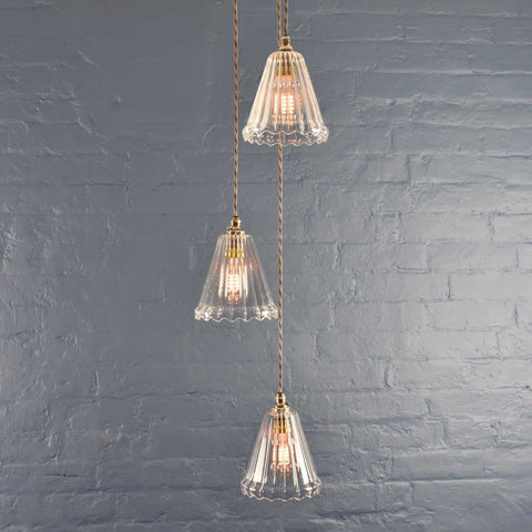 Rye small ribbed glass shade cluster pendant light with three hand-blown glass shades and adjustable flex cables against a gray brick wall background