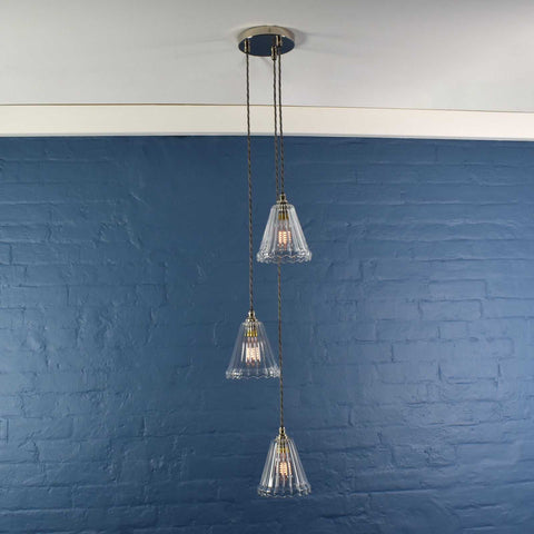 Rye Small Ribbed Glass Shade cluster pendant light with three clear ribbed glass shades hanging at varying lengths against a blue wall