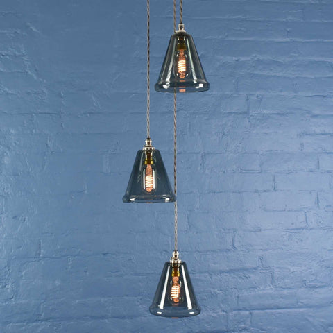 Rye small smoked glass shade cluster pendant light with three hand-blown glass shades and adjustable cords against a blue brick wall background