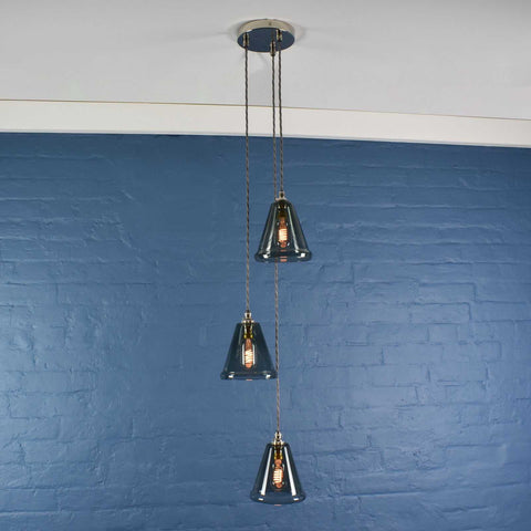 Rye small smoked glass shade cluster pendant light with three hand-blown glass shades hanging against a blue brick wall