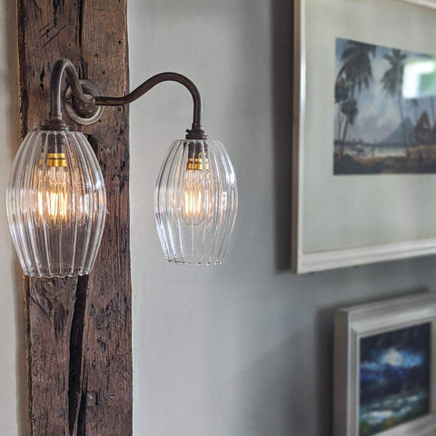 Camber small ribbed glass shade wall light with hand-blown ribbed glass and bronze metal arm mounted on rustic wooden beam in a modern interior.