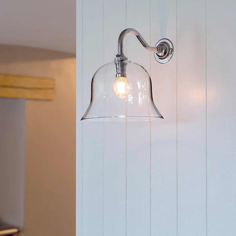 Bodium medium clear glass shade wall light with polished nickel finish and exposed bulb mounted on white paneled wall