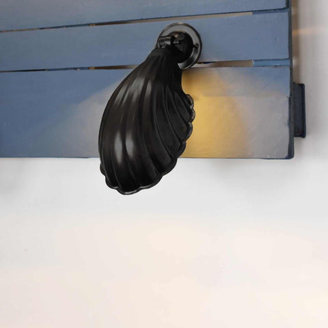 Hadlow Adjustable Brass Shell Wall Light in matte black finish mounted on blue wooden panel illuminating wall.