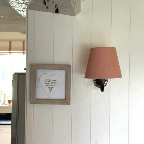 Finberry Pink Linen fabric shade wall light with brass swan neck fitting on white wooden wall next to framed artwork
