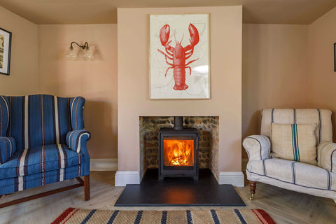 A wall Light in a cosy living rooom with two armchairs and a log burner fire.