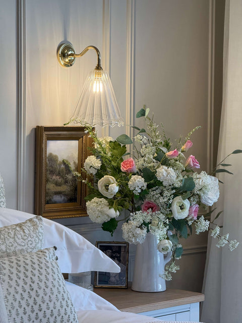 Rye Medium Ribbed Wall Lighting by a bed with flowers.  Swan Neck fitting and polished brass.