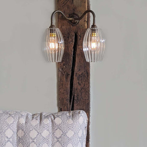 Camber Small Ribbed Glass Shade wall light with two fluted oval glass shades mounted on a rustic wooden beam above a patterned cushion