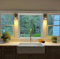 Pair of Accra Traditional Small Brass Spotlights in antique brass finish mounted either side of a window above a kitchen sink, providing focused task lighting in a cosy traditional kitchen interior.