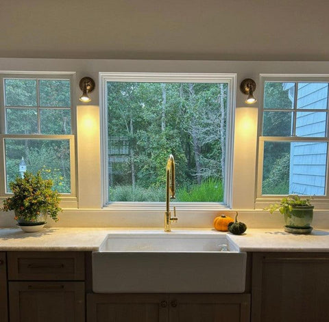 Pair of Accra Traditional Small Brass Spotlights in antique brass finish mounted either side of a window above a kitchen sink, providing focused task lighting in a cosy traditional kitchen interior.