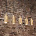 Ennis IP44 Spot Pendant Light set with sleek cylindrical brass fixtures hanging against a rustic brick wall