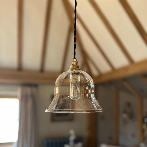 Bathroom pendant light with adjustable clear glass shade and brass fittings, hanging from a twisted cord in a rustic interior.