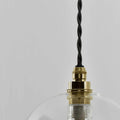 Bathroom pendant light with clear glass shade, brass fixture, and adjustable black twisted cord.