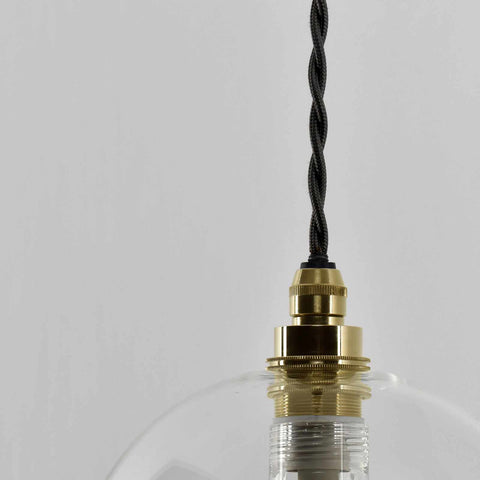 Bathroom pendant light with clear glass shade, brass fixture, and adjustable black twisted cord.
